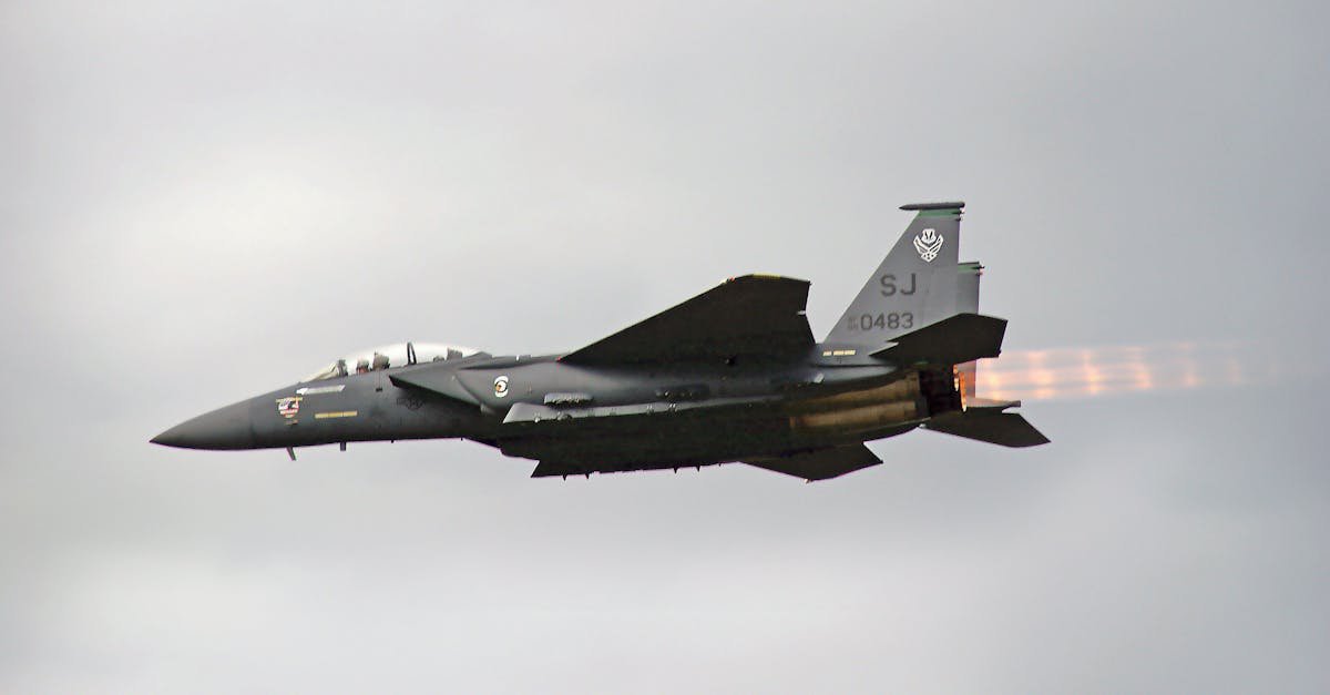 Dramatic view of F-15 fighter jet flying outdoors, showcasing afterburners against a cloudy sky.
